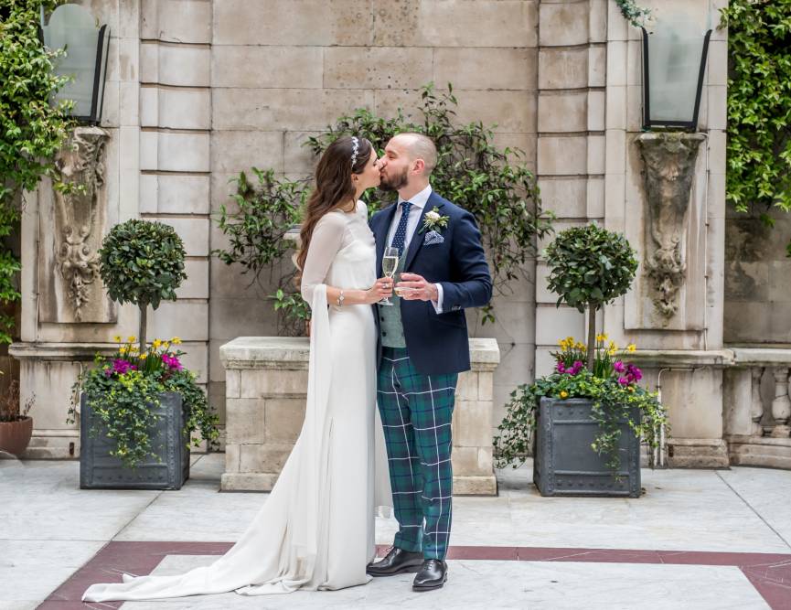 A joyful moment as the bride and groom kiss, framed by a picturesque fountain, celebrating their love and commitment.