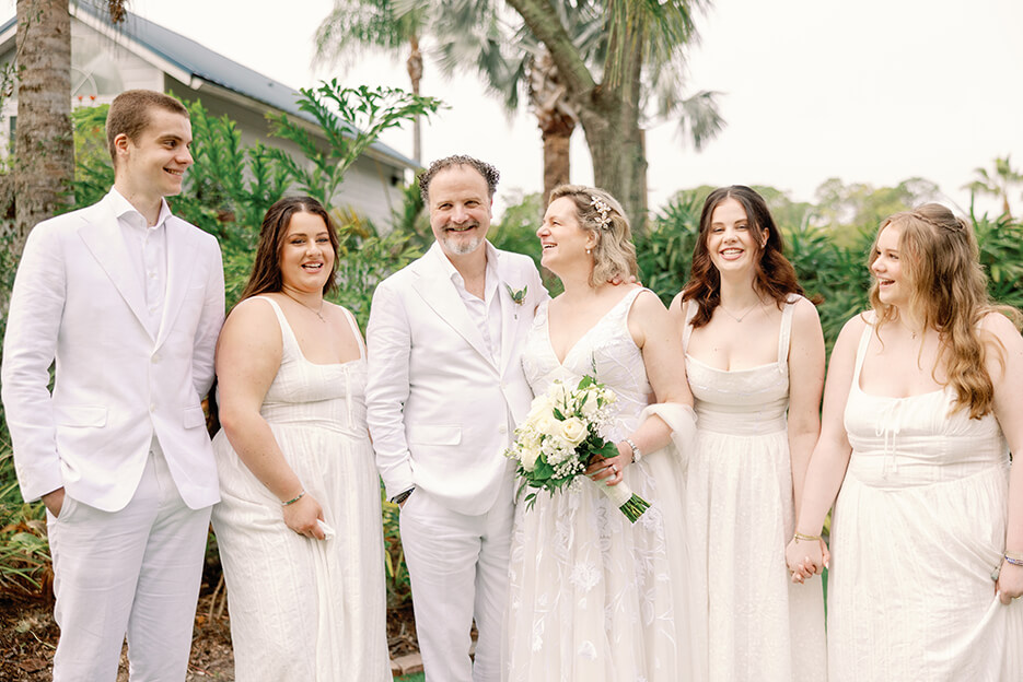 The bride and groom pose with their wedding party, radiating happiness in a beautiful garden backdrop.