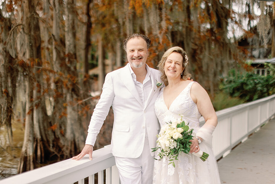 A bride and groom stand together on a bridge, smiling for a romantic photo on their wedding day.