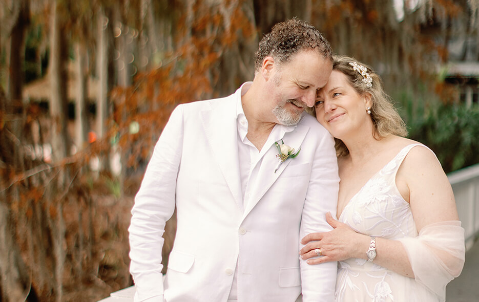 A bride and groom stand together on a bridge, smiling for a romantic wedding photo.