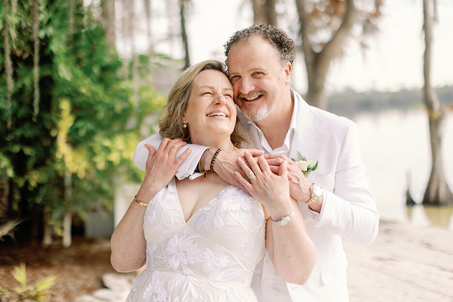 A couple in wedding attire embraces on a serene beach, surrounded by the beauty of the ocean and soft sand.